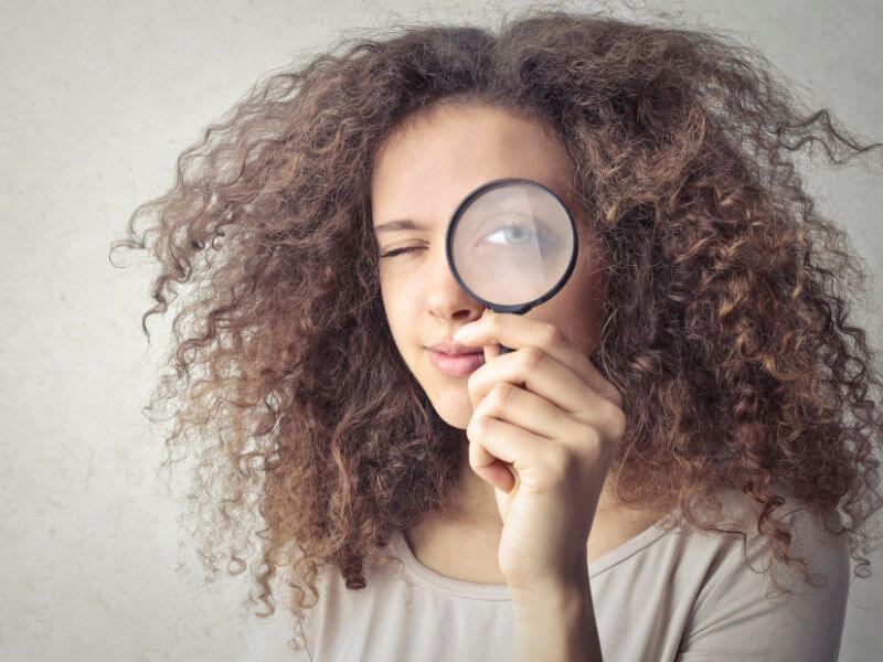 eine Frau, die ein Vergrößerungsglas über ihr Auge hält
